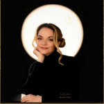 Portrait of author and memoirist Sophy Le’coa, seated in soft light against a dark background, wearing black and resting her chin on her hand.
